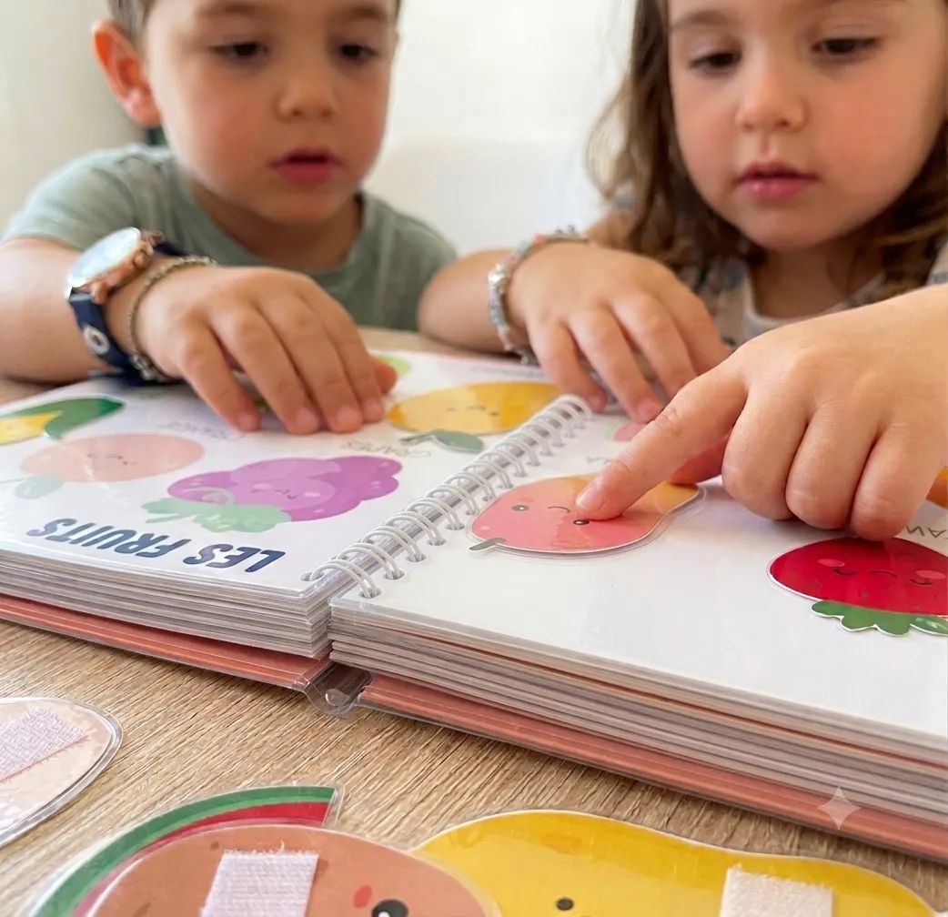Deux enfants placent des pièces amovibles sur la page « Les fruits » d'un cahier Doudie's à reliure spirale et pages plastifiées